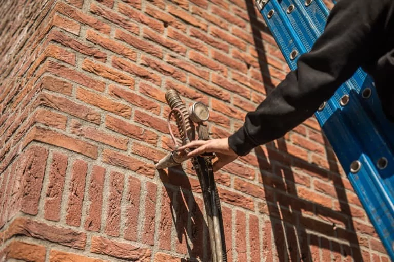 Medewerker van Kok Groep brengt isolatie aan in een gevel met behulp van een spuitpistool en slang.