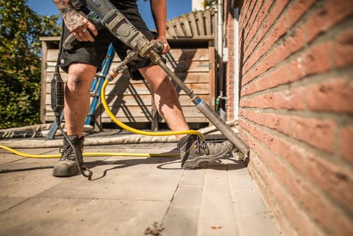 Medewerker van Kok Groep boort gaten in een gevel om isolatiemateriaal aan te brengen.
