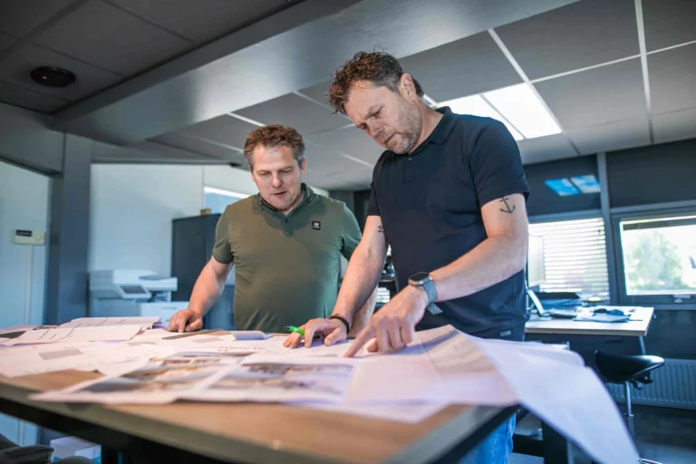 Mannen die bezig zijn aan een bureau met papieren hierop.
